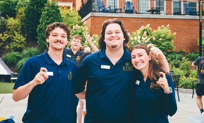 Group of three orientation leaders making a hook symbol with their fingers.