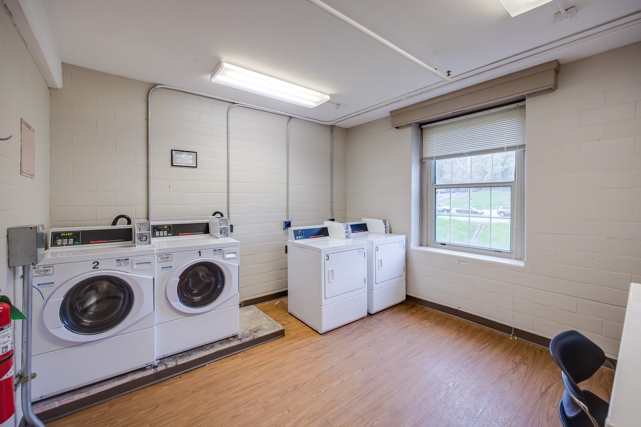 Washers and dryers are lined up on the wall of a laundry room with tan walls, a tile floor, and a folding counter.