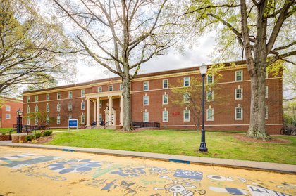 Exterior view of Nell J. Dossett Hall, a brick residential hall with tan columns by the door, and landscaped with trees.
