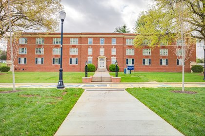 An exterior view of West Hall, a large brick residential building with iron lamps and sidewalk out front.