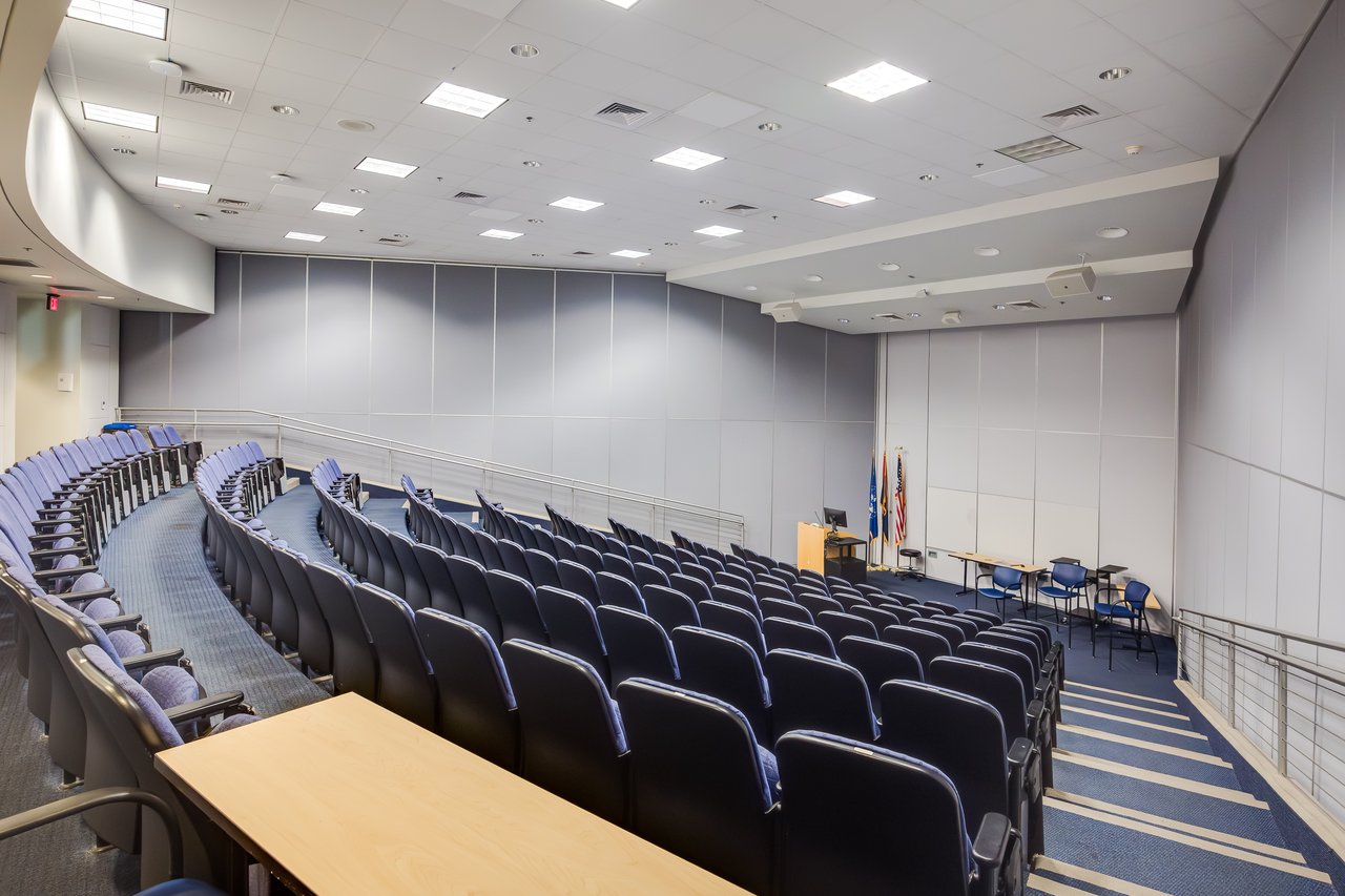 Interior of a modern lecture hall with tiered seating, a podium, and a clean, minimalist design.