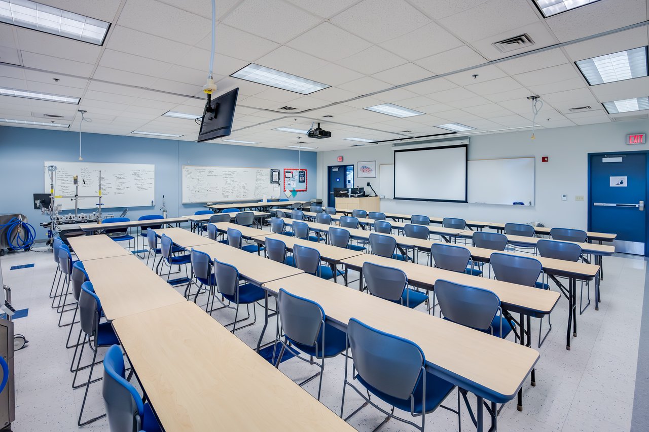 A classroom with rows of tables and chairs, screens, and whiteboards, arranged for learning.