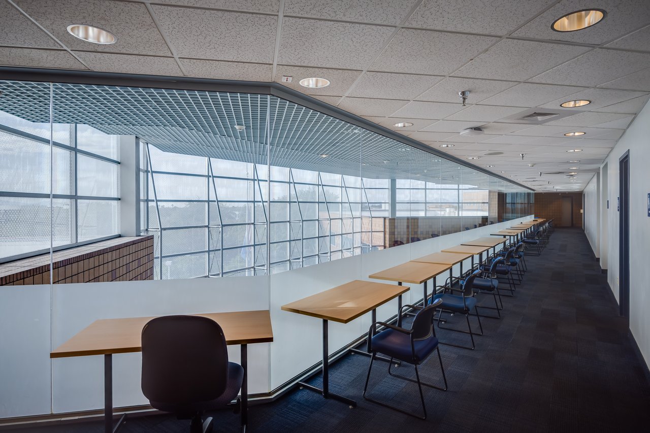 A spacious hallway with several tables and chairs, featuring large windows that let in natural light.