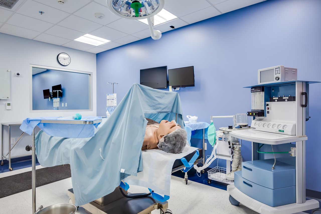 A medical simulation room with an operation table, a manikin covered by a drape, and medical equipment.