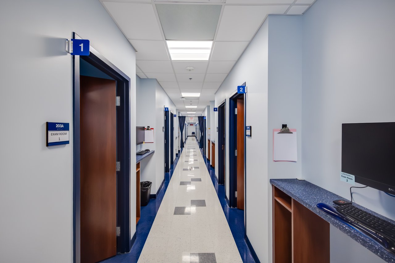 A clean, well-lit hallway in a medical facility with exam rooms and a workstation along the walls.