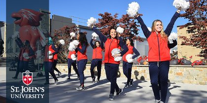 Cheerleaders in red jackets perform with pom-poms outdoors at St. John's University, with a mascot in the background.